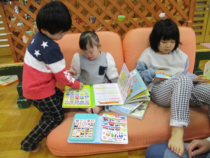 三人の子どもがカラフルな絵本や知育本を広げて読んだり見せ合ったりしている写真
