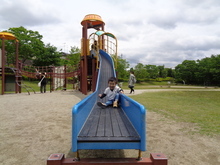 青い滑り台の下部に幼い子どもが滑っている様子を滑り台の降り場の正面から撮影した写真