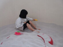 女の子が室内の砂場で、砂遊び用のおもちゃを持って遊んでいる様子の写真