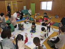 星柄のシートの上に複数の子どもやクリスマス風の衣装を着た人達がカラフルなボールで遊んでいる様子が見える写真