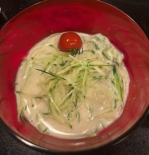 赤い器に白く濃厚なスープをまとったかっぱ麺が盛られ細切りきゅうりがたっぷり覆い上にミニトマトが添えられた料理の写真