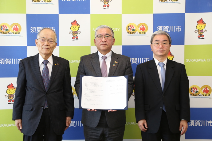 須賀川市バックボードの前で、中央の橋本市長が文書を掲げ、その両サイドに福島労働局長、須賀川商工会議所会頭が立ち記念撮影をしている写真