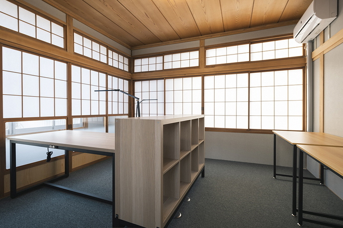 木の温もりが感じられる天井や障子に囲まれた和風の空間に、モダンなデスクやオープンシェルフが配置され、伝統的な造りと現代的なオフィス家具が調和した機能的な個室の写真