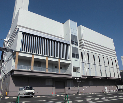 広い駐車場の横に、1階部分がグレー、2階以上が白の外壁で、2階の一部にバルコニーが設けられた四角い建物が建つ、須賀川地方衛生センターの外観写真