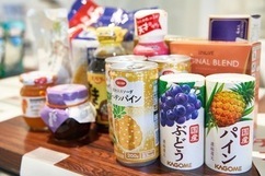 木製のテーブルの上に、カゴメの国産ぶどうやパインの缶ジュース、ジャムの瓶、調味料、袋詰めの食品など、フードドライブに寄付するために集められた様々な未開封の保存食品が整然と並べられている写真
