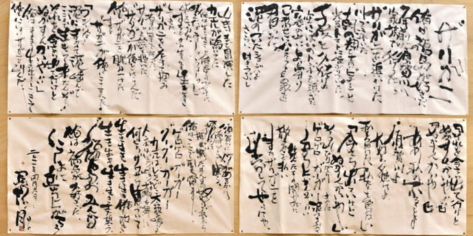 描かれた書道作品が四枚が横2枚、縦2列に掲示され、力強い筆致で多くの文字がびっしりと書き込まれた様子を捉えた写真