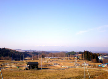 冬枯れの茶色い大地が広がり遠くの山々を見渡せる風景を、少し高い丘から撮影した冬のガーデンタウン虹の台の写真