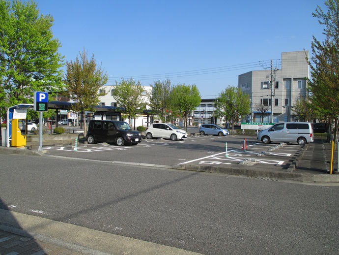 周囲を木々に囲まれ、複数の車が駐車している、パーキングメーター付きの駐車場の写真