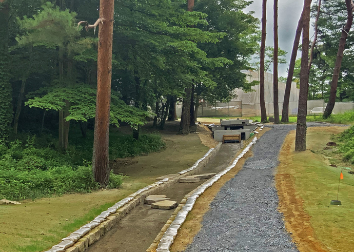 松林の中に整備された砂利道に沿って水路が設置された、せせらぎ水路浄化システムの写真