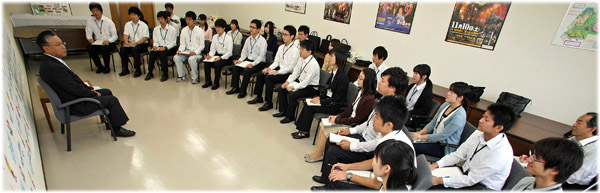 明るい会議室でスーツ姿の市長が椅子に座り、半円状に並んで座るシャツやスーツ姿の男女十数名の若者たちと対面しながら話し合いを行っている、市長との行政経営意見交換会の様子の写真