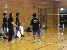 バドミントンコートのネット付近に、ラケットを持った複数の参加者が集まっている様子の写真