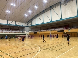 天井の高い体育館に設置された複数のバドミントンコートで、参加者たちが練習を行っている写真