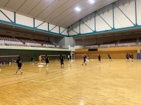 黒いシャツを着たたくさんの参加者たちがバドミントンの練習を行っている様子を遠目から撮影した写真