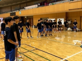 床に多数のシャトルが散らばり、黒いシャツを着た参加者たちがノックを受けている様子の写真