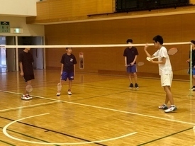 白いシャツを着た男性が、ネット越しに立っている3人の参加者に向かって指導をしている様子の写真