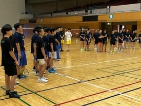 体育館で黒いウェアを着た参加者たちがラケットを手に整列している写真