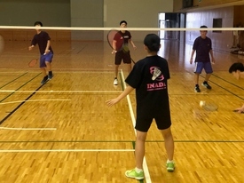 バドミントンコートで、ネット越しにペアでの練習をしている様子の写真