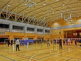 バドミントンのネットが張られた体育館に、たくさんの参加者が整列している様子の写真