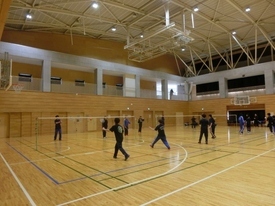 ネットが張られた3面のコートで、バドミントンの練習をしている様子の写真