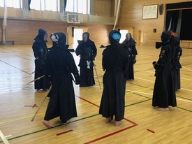 広々とした体育館で、剣道着と防具を身に纏った複数の生徒たちが円陣を組むように集まっている写真