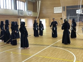 明るい光が差し込む体育館で、防具と剣道着を着用した多くの生徒たちが、指導者の前に整列して真剣な面持ちで話を聞いている写真