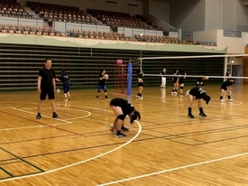 広い体育館で黒いウェアを着た生徒がボールを使った練習を行っている写真