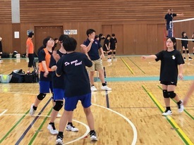 体育館にて、黒い練習着を着用した女子バレーボール選手たちがコート内で会話を交わしている様子の写真