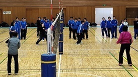 体育館で、青いジャージを着用した複数の生徒たちがコート上で練習をしている写真