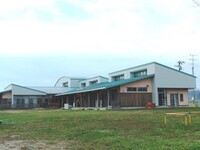 芝生が広がる敷地に建つ緑色の屋根と薄い白色の外壁が特徴的な木造風の平屋建て校舎の写真