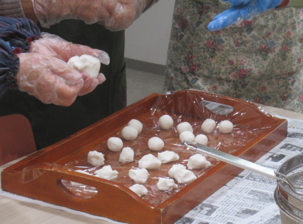ビニール手袋をした手で白い生地を丸め、木製の盆に並べていく様子を写した写真