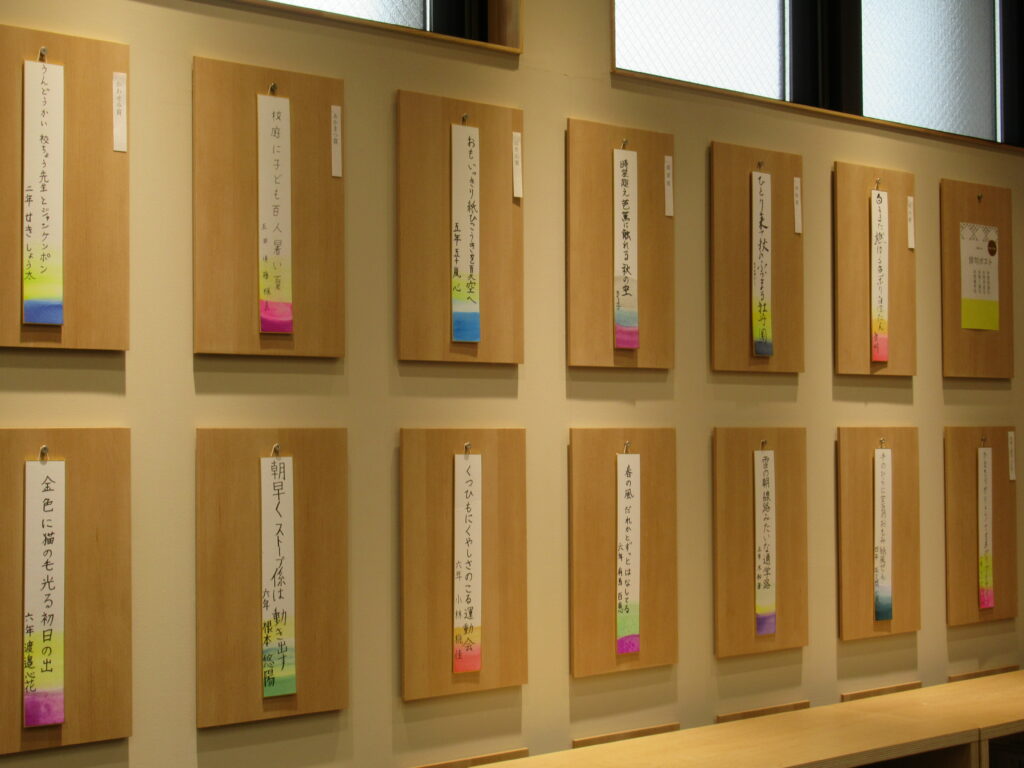 壁一面に木製パネルが整然と並び、それぞれに俳句が書かれた短冊が掛けられて展示されている写真