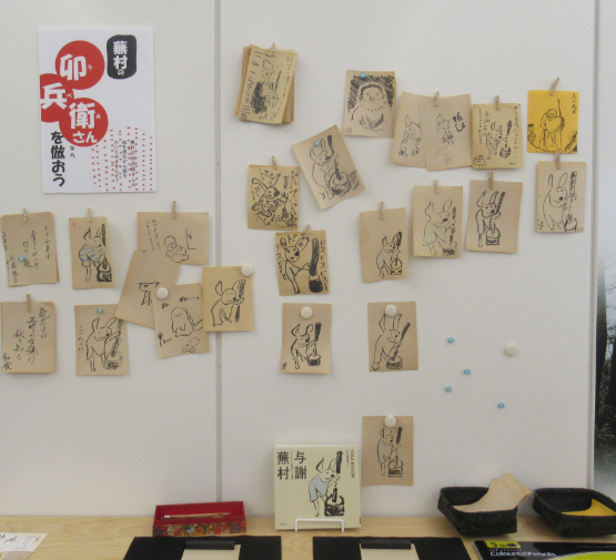 「卯兵衛さんを倣おう」のチラシが貼られた壁に、絵が描かれた複数のカードがクリップで留められている写真