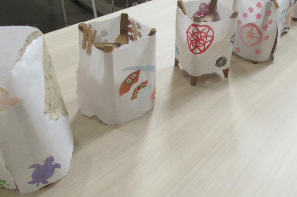 糸巻きに切り紙などで装飾を施した和紙を巻いた、手作りの行灯が複数並んでいる写真