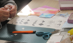 見本や色紙、ハサミ、カッターナイフなどが置かれた作業台の上で、細かな紙片を扱い作業をしている手元を写した写真