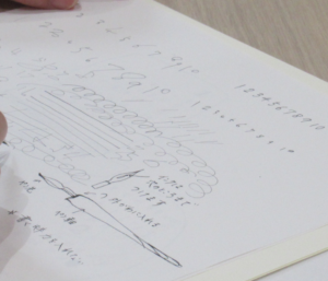 白い紙に手書きの数字や波線、渦巻き状の線が並び、下部にはつけペンの構造や使い方の解説イラストとメモが添えられている様子を斜め上から撮影した写真