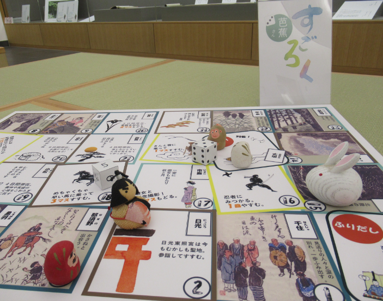 畳の上に並べた名所や人物が描かれたすごろく盤の上に小さなぬいぐるみ駒が置かれた展示の写真