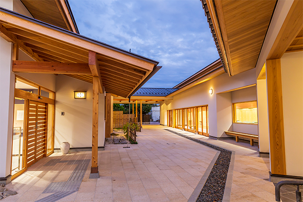 夕暮れ時の淡い空の下、美しい木造の深い軒下と石畳の通路が続き、温かな明かりが灯っている風流のはじめ館の中庭通路の外観写真