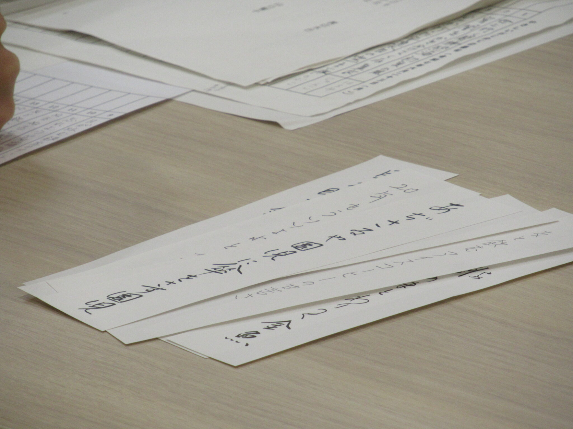 資料を広げた机の上に、俳句が書き込まれた短冊が重なるように置かれている写真