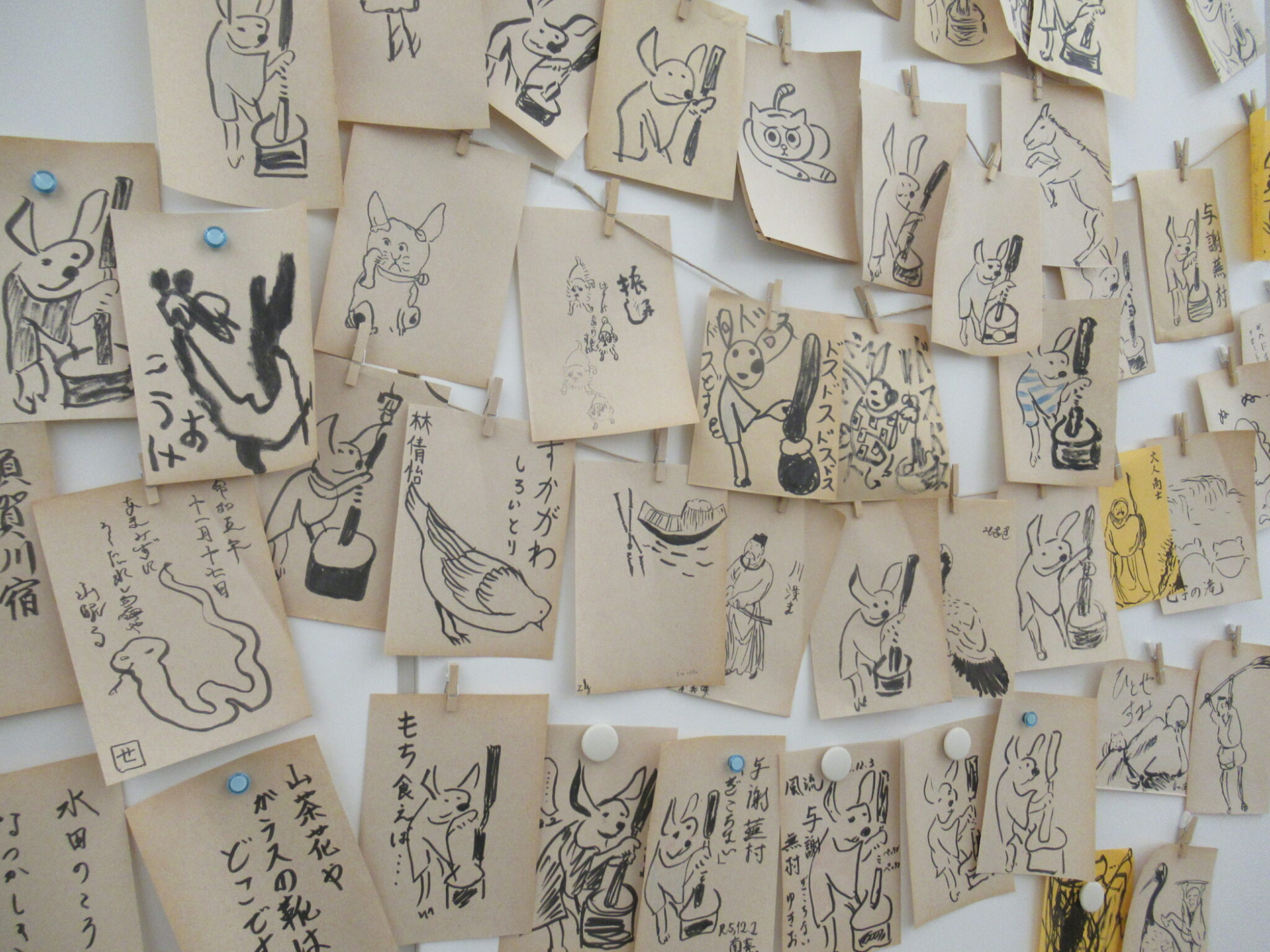 餅をつくウサギなどが黒で描かれた、たくさんの正方形の小さな紙が、壁一面にクリップで留められている写真