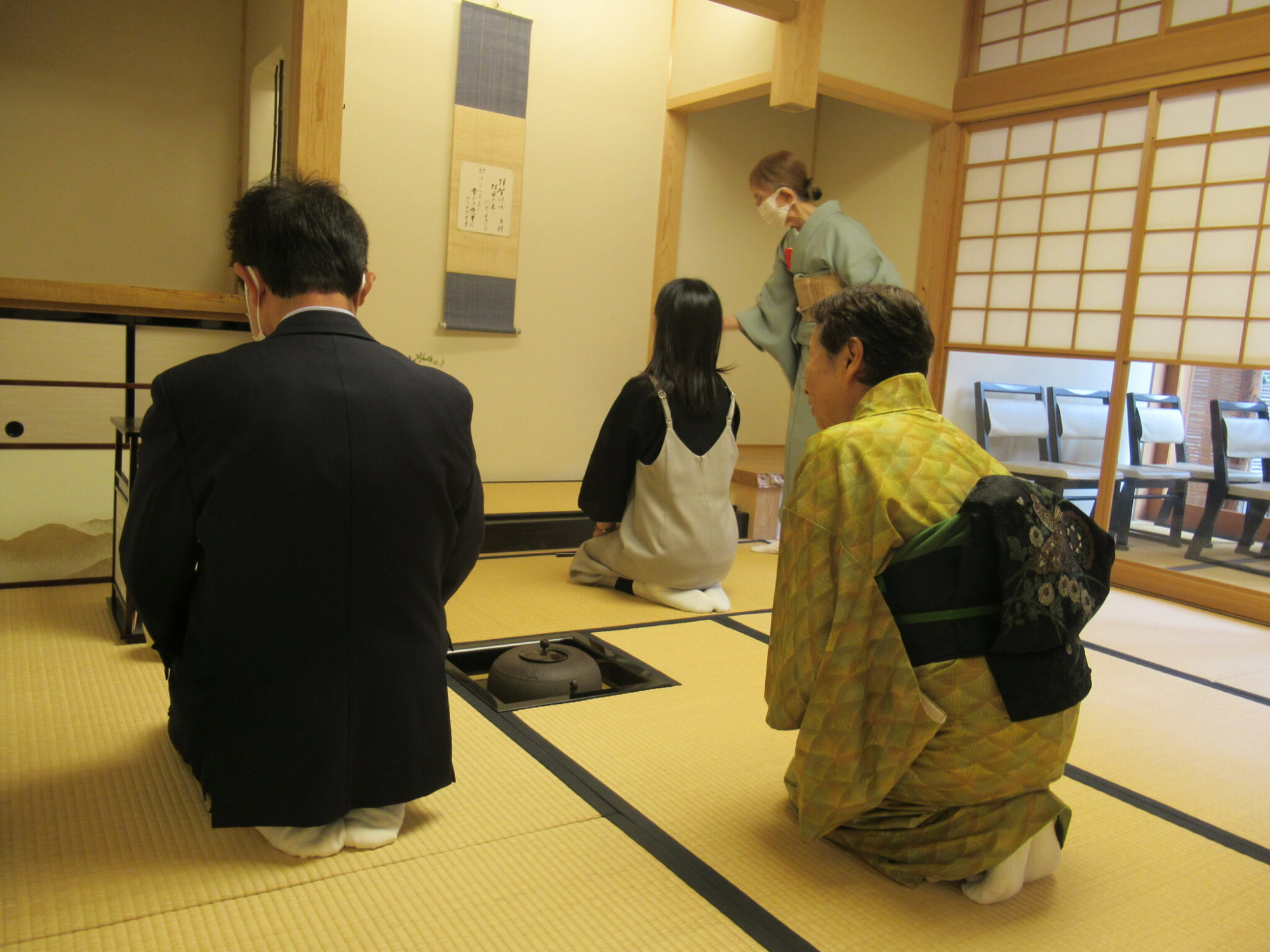 畳の茶室で着物姿の指導者のもと参加者が炉の前に正座し道具の扱いを丁寧に学んでいる静かな雰囲気の中の様子の写真