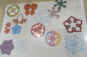 白い紙の上に、多彩な色と形の切り紙が並べられた写真