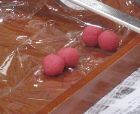 食品ラップを敷いた木製の盆の上に丸められた赤い生地が四つ並んでいる写真