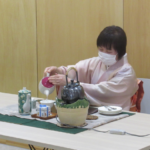 和装の女性が卓上の茶器に丁寧に茶を注いでいる写真