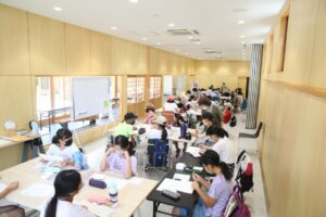 広い室内で、たくさんの子どもたちが複数のテーブルを囲んで座っている写真