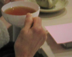 琥珀色の茶が入ったティーカップを持ち上げた手元の写真