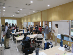 広い部屋で、子どもたちが席に着き、ホワイトボードの横に並んで立った発表者たちの方を見ている発表の様子の写真