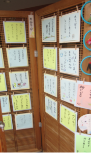 中央に「低学年の部」の短冊が貼られた格子状の木製パネルに、俳句やイラストが手書された様々な色の色紙がたくさん並んでいる展示の様子の写真