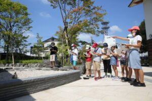 屋外の石庭園の前に集まった子どもたちが、ノートを手に景色を観察している様子の写真