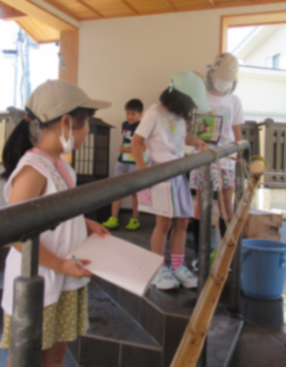 屋根付きのスペースで、数人の子どもたちが、竹の上を水が流れる様子を手すり越しに見ている様子の写真