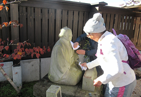 木柵の前で二人が布を使って座った石像を丁寧に拭き清めながら手入れを行っている様子の写真